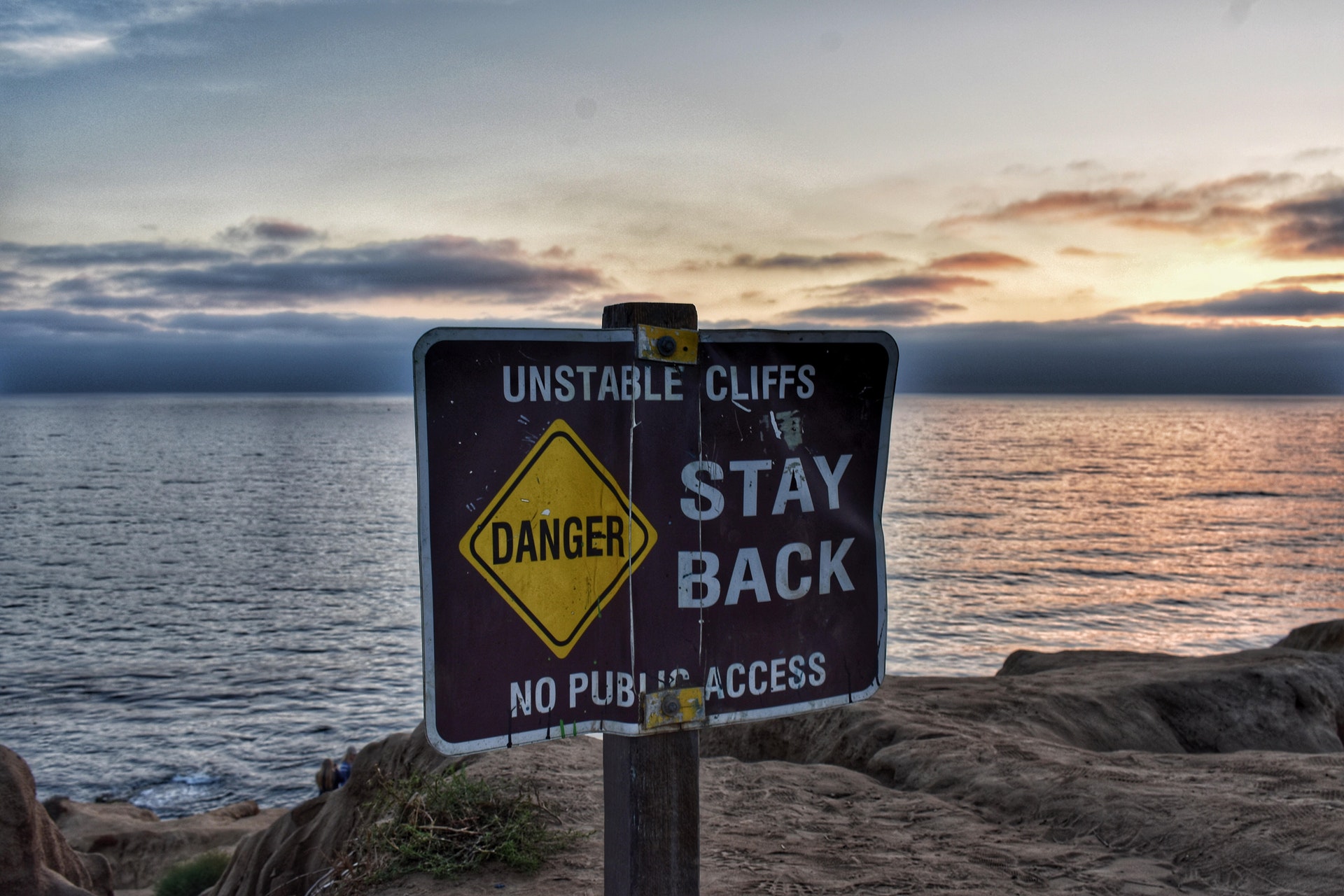 Photo of seaside cliff with sign: Unstable cliffs. Danger. Stay back. No public access.
