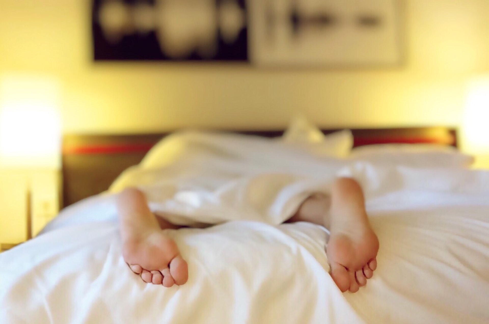 Photo of person faced-down in bed with just their feet showing from under the covers.